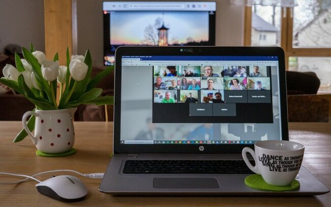 Labtop zu Hause mit Kaffeetasse. Teilnehmende an einer Videokonferenz auf Kacheln am Bildschirm sichtbar.